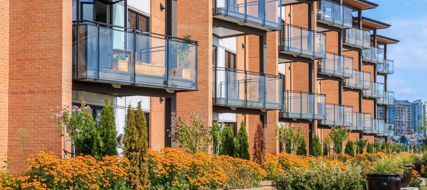 Moderne leilighetsbygg med flere balkonger og blomstrende hage foran fasaden.