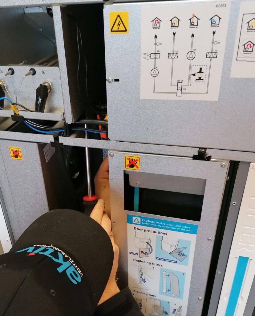 Person justerer komponenter inne i ventilasjonsaggregat med skrutrekker.