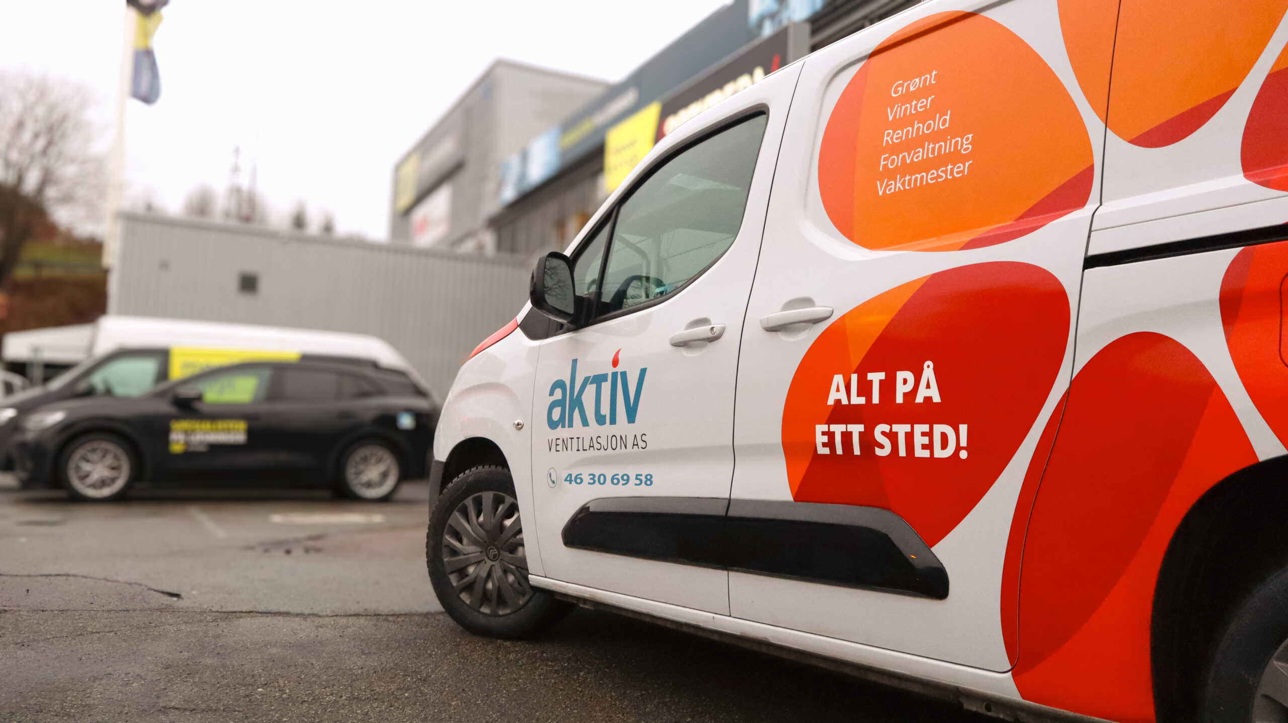 Hvit varebil med Aktiv Ventilasjon AS-logo parkert ved bygg.