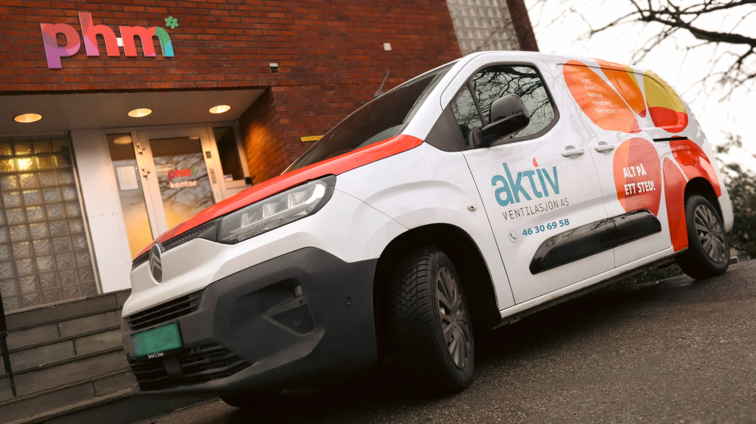 Hvit varebil med Aktiv Ventilasjon AS-logo parkert foran phm-bygning.